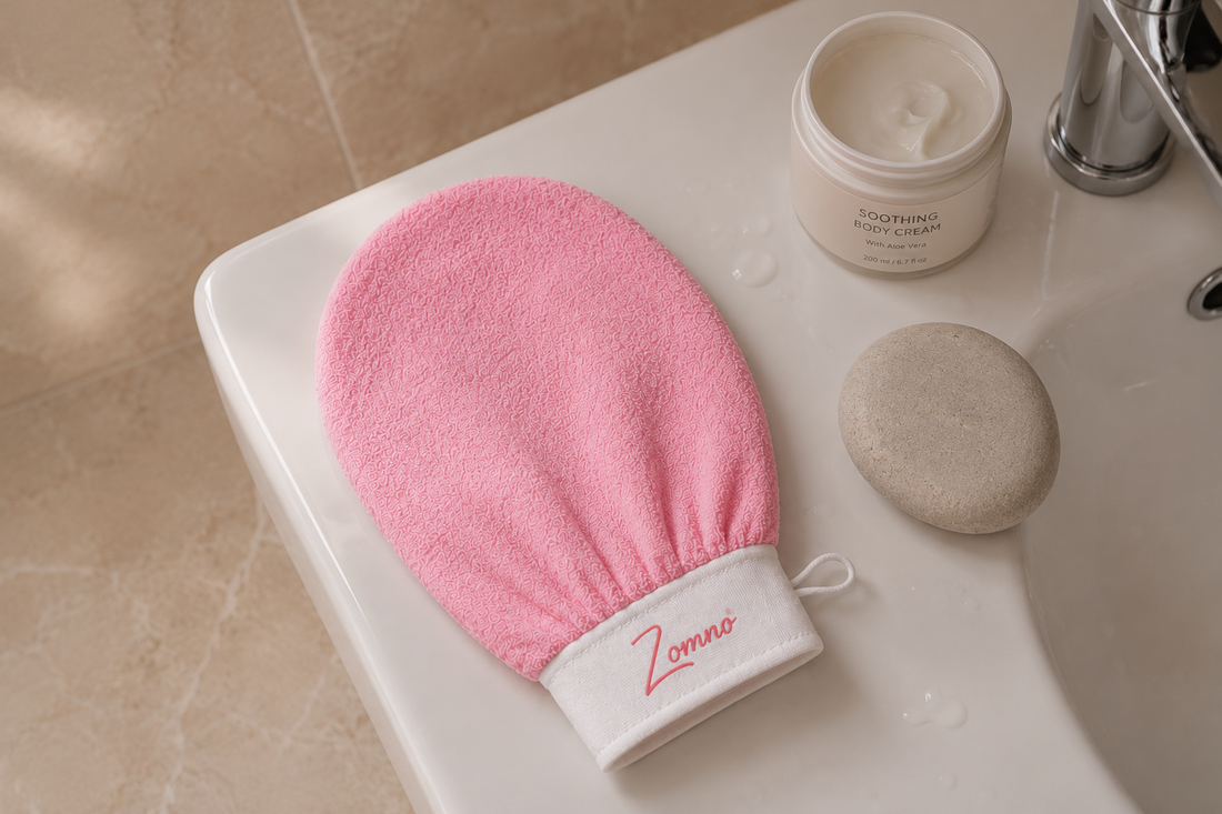 Zomno™ exfoliating glove resting on a clean white towel next to a simple ceramic jar of moisturizer, soft morning light from a window, no people, minimal and calm